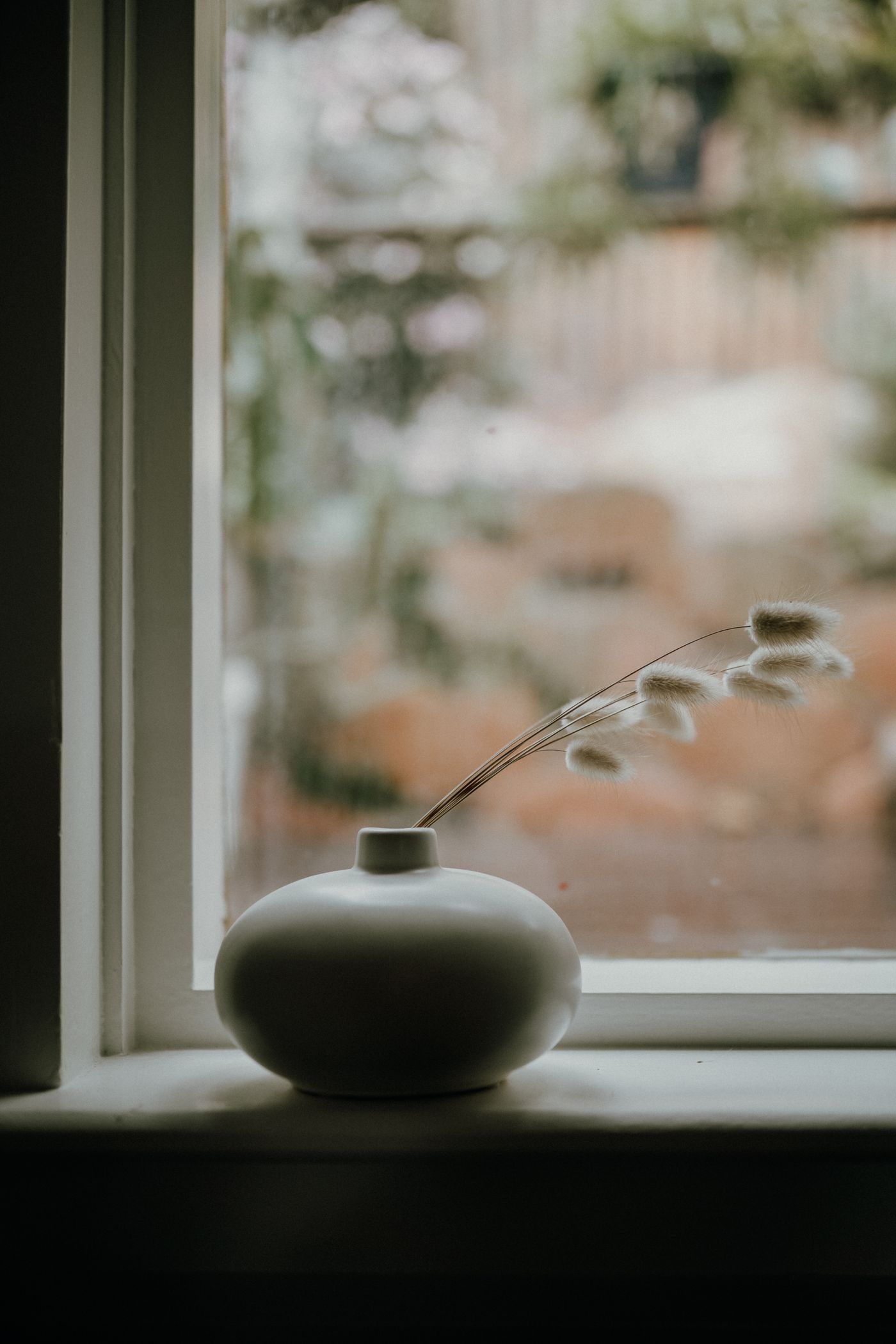 Delicate flowers in a white ceramic vase on a windowsill